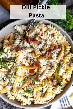 a white bowl filled with pasta and bacon on top of a gray table next to silverware