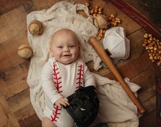 a baby is sitting on the floor holding a baseball glove and smiling at the camera