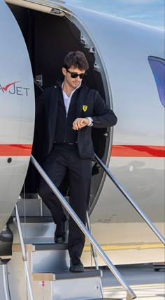 a man in a suit and sunglasses stepping down the stairs from an airplane to his plane