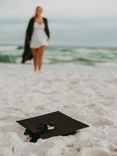 a graduation cap on the beach with a woman walking in the water behind it,