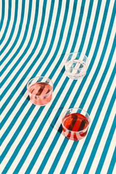 two wine glasses sitting on top of a blue and white striped table cloth next to each other