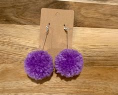 the purple pom - pom earrings are displayed on a wooden table next to a card