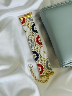 a cross stitch bracelet laying on top of a white blanket next to a wallet and chain