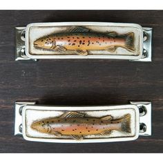 two fish shaped metal cabinet pulls on a wooden surface with holes in the center and bottom