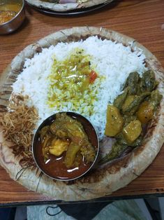 a wooden plate topped with rice and meat next to other dishes on a wood table