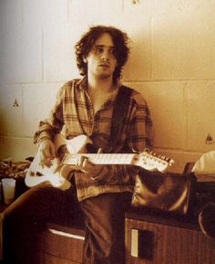 a young man sitting on top of a bed holding an electric guitar