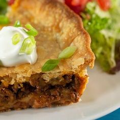 a piece of meat pie with sour cream on top and salad in the back ground