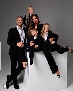 a family posing for a photo in suits and ties on a white pedestal with their children