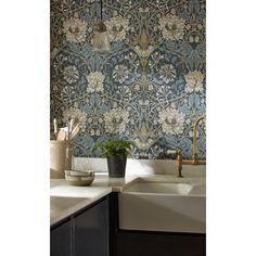 a kitchen sink under a hanging light next to a wall papered with blue and white flowers