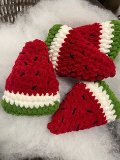 three knitted watermelon hats sitting on top of a pile of white wool