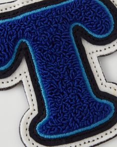 the letter t is made out of blue and white material with black stitching on it