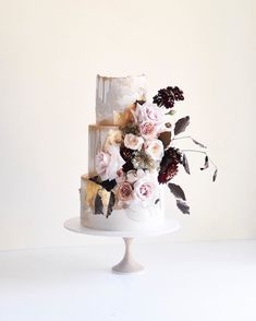 a three tiered cake with flowers and leaves on top sits on a white pedestal