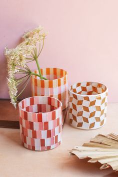 three different colored cups sitting on top of a table next to a flower vase and fan