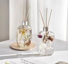 two glass vases filled with flowers on top of a white table next to a book