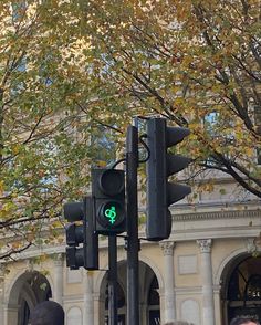 two traffic lights are green in front of a building and trees with leaves on it