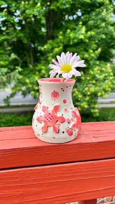 a white and pink flower vase sitting on top of a red bench