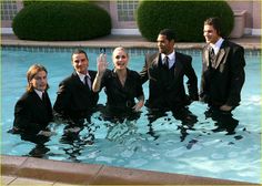 a group of people in suits standing in a pool waving at the camera with their hands up