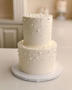 three tiered white wedding cake with pearls on the top and bottom, sitting on a table