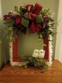 a red and green christmas wreath on top of a wooden table next to an owl