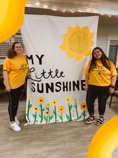 two women in yellow shirts standing next to a banner that says my little sunshine on it