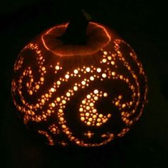 a carved pumpkin with an intricate design on it's face, lit up in the dark