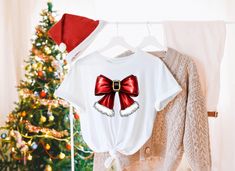 Get into the holiday spirit with this adorable Festive Red Bow Christmas Shirt! 🎄 Featuring a bold, festive bow with a touch of Santa's classic style, this tee is perfect for celebrating the season in style. Whether you're cozying up at home or attending a holiday party, this soft, comfortable shirt is the perfect festive touch. 🎁 Makes a great Christmas gift for your loved ones or for yourself to rock that holiday cheer! Wear it to family gatherings, Christmas shopping, or simply lounging around with a cup of cocoa. Red Bow Christmas, Holiday Graphic Tees, Bow Christmas, Cute Christmas Gifts, Christmas Vibes, Great Christmas Gifts, Red Bow, Cute Christmas, Cozy Christmas