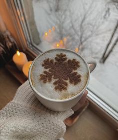 a person holding a cup of coffee in front of a window with candles on it