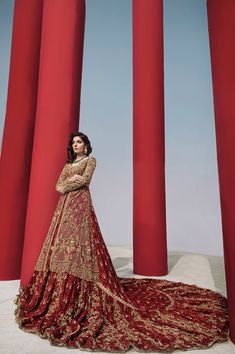 a woman in a red and gold dress standing next to some tall red pillars with columns behind her