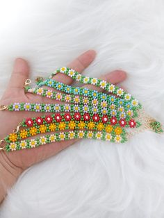 a hand is holding several beaded bracelets in different colors and designs on white fur