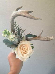 a hand holding a flower arrangement with antlers and flowers