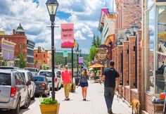 people walking down the sidewalk in front of shops on a sunny day with their dog