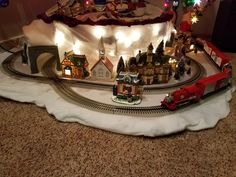 a toy train set up in front of a christmas tree with lights and decorations on it