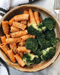 a bowl filled with broccoli and pasta on top of a table next to a fork