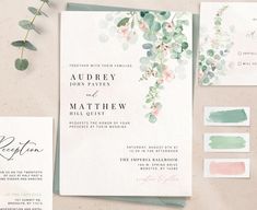 the wedding stationery is laid out on top of each other, with greenery and watercolors