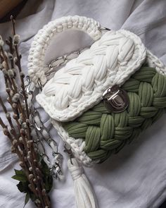 a white purse sitting on top of a bed next to a branch with flowers in it