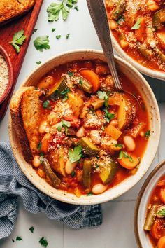 two bowls filled with vegetable stew next to bread and parmesan cheese on the side