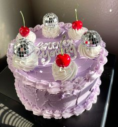 a purple cake with white frosting and cherries on top is decorated with disco balls