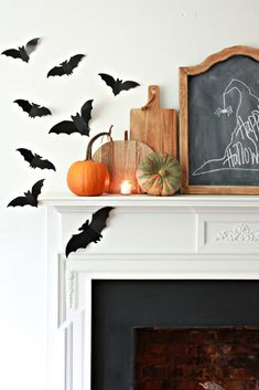 a fireplace mantle decorated with bats, pumpkins and a chalkboard for halloween written on it