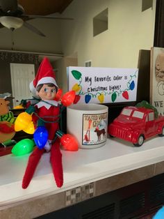 an elf is sitting on top of a shelf next to christmas lights and a coffee mug