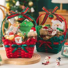 two baskets filled with christmas treats sitting on top of a table next to small figurines