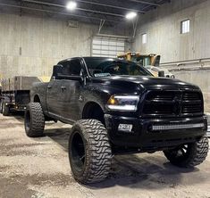 a large black truck parked inside of a garage next to a dump truck with big tires