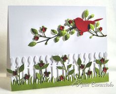 a red bird sitting on top of a green plant next to a white picket fence