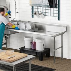 a man in blue pants and yellow gloves is washing dishes on a stainless steel sink