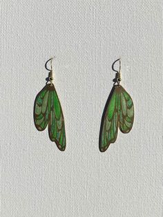 a pair of green butterfly wings hanging from earwires on a white cloth background