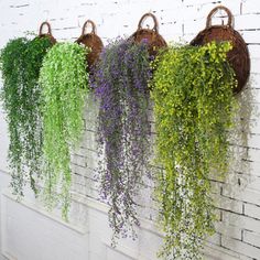 four hanging baskets filled with green and purple flowers next to a white brick wall covered in wicker baskets