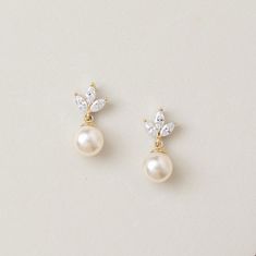 two pairs of pearl and crystal earrings on a white surface, one with a gold plated ear pin