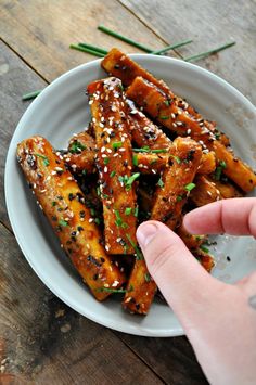 someone is reaching for some chicken wings on a plate with sesame seed sprinkles