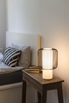 a lamp sitting on top of a wooden table next to a white headboard and pillows