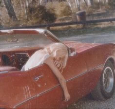 a woman leaning on the hood of a red car