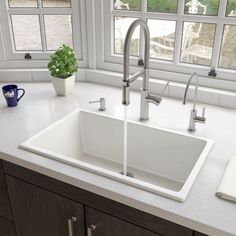 a white kitchen sink sitting under a window next to a counter top with a potted plant